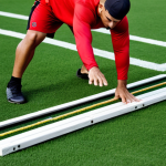 A focused male baseball player in full, professional athletic training attire, executing a dynamic agility ladder drill on a pristine green baseball field. His body shows perfect anatomy and correct proportions, with well-formed hands and proper finger count in a natural pose. The scene is captured with professional photography, showcasing his determination and athletic prowess under natural lighting. This is a high-quality, safe for work, appropriate content, fully clothed, professional image.
